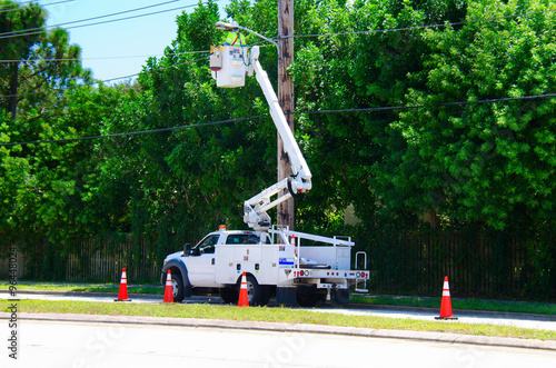 Electrician working on high power lines from a lift on the back of a truck that is parked in the street and surrounded by warning cones