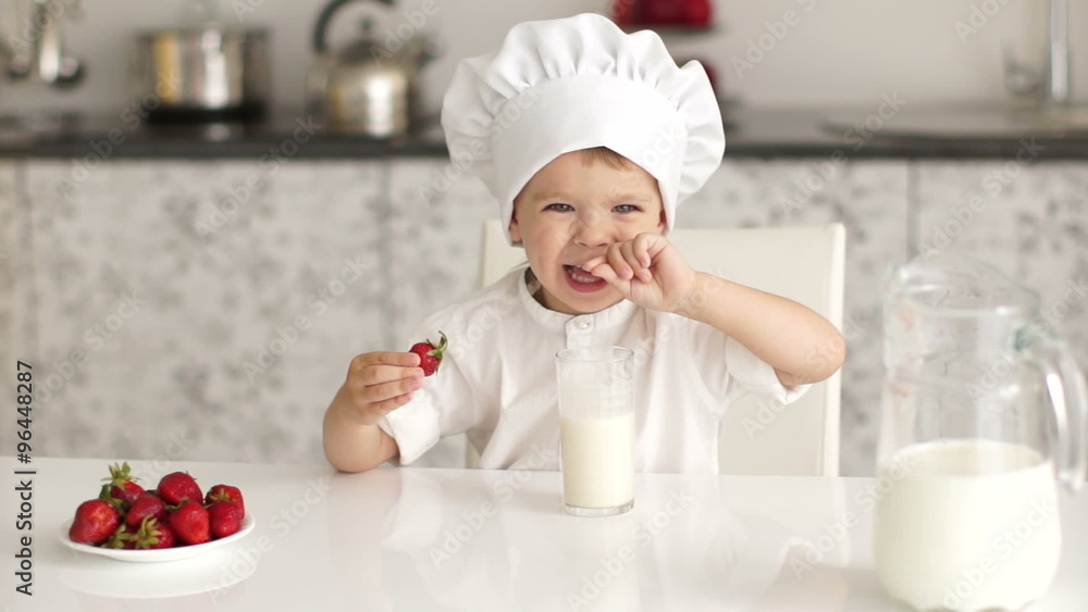 Little boy sitting at table and eating strawberries