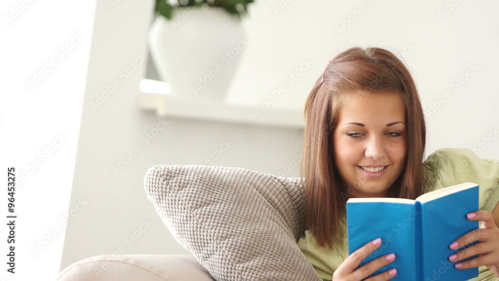Pretty girl relaxing on sofa reading book and smiling Pretty girl relaxing on sofa reading book and smiling