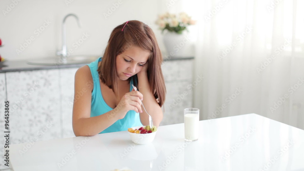 Young woman expressing dissatisfaction sitting at kitchen table with bowl of salad Young woman expressing dissatisfaction sitting at kitchen table with bowl of salad