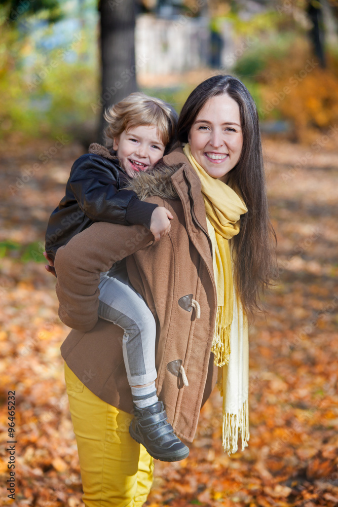 Fototapeta premium Happy mother piggybacking her son in autumn.