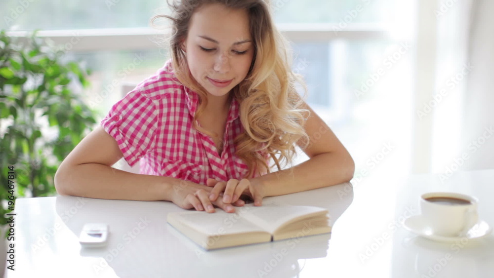 Attractive young woman sitting at table with cup of coffee and reading book Attractive young woman sitting at table with cup of coffee and reading book