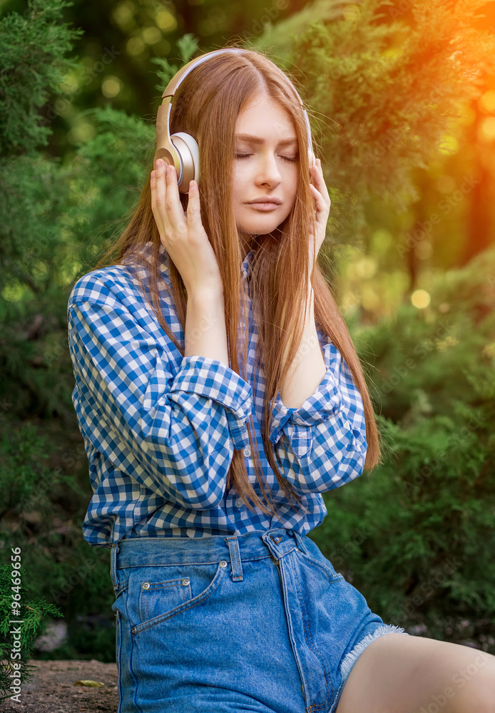 Young woman cute brunette girl sitting on stone headphones Young woman cute brunette girl sitting on stone headphones