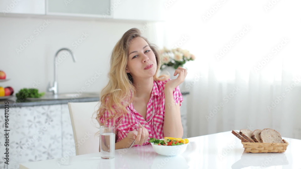 Pretty girl in kitchen eating vegetable salad and smiling at camera