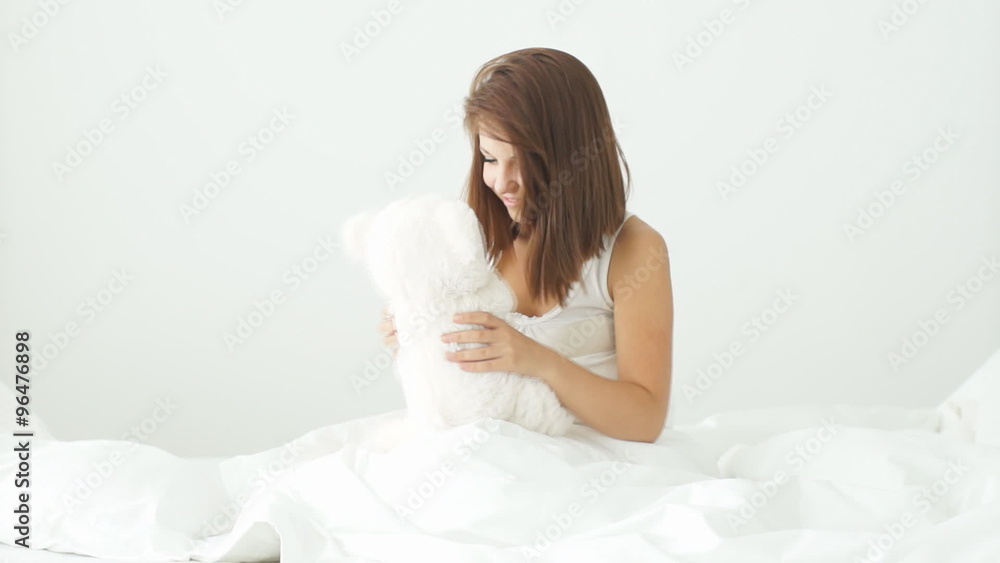 Young woman sitting on bed playing with teddy bear and smiling at camera Young woman sitting on bed playing with teddy bear and smiling at camera