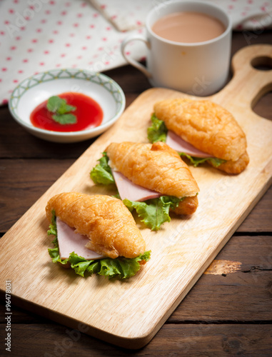 Fresh croissant ham and salad leaf with sauce on dark wooden bac
