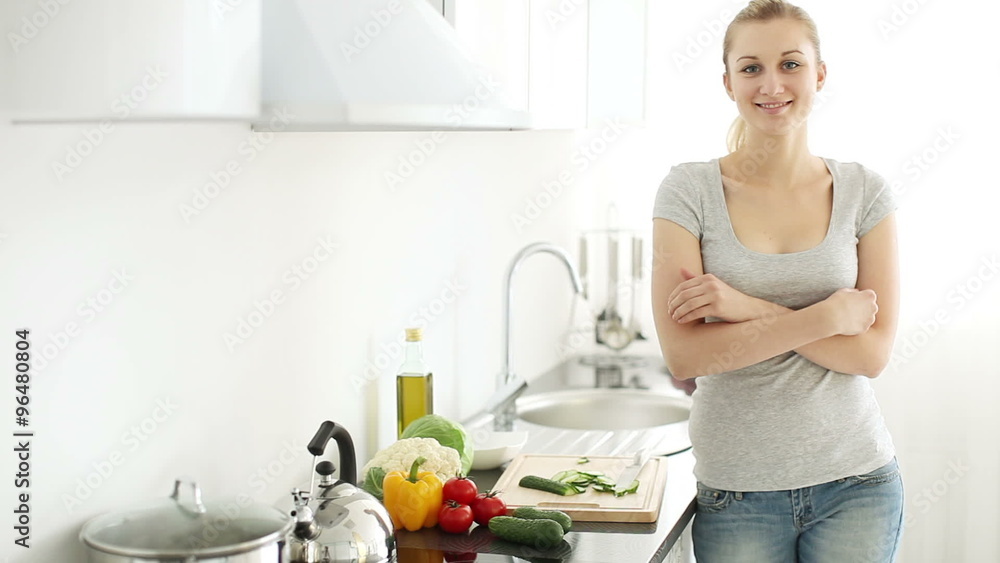 Pretty young woman standing in kitchen cutting vegetables turning around and smiling at camera Pretty young woman standing in kitchen cutting vegetables turning around and smiling at camera