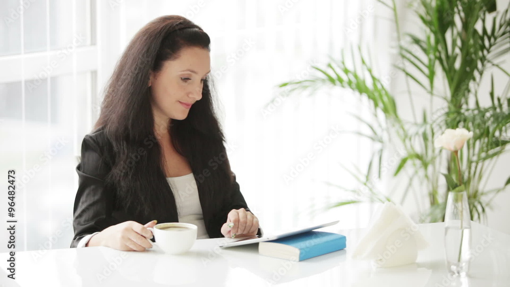 Beautiful young woman sitting at table drinking coffee using touchpad smiling and looking at camera Beautiful young woman sitting at table drinking coffee using touchpad smiling and looking at camera