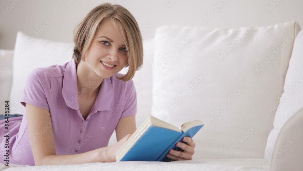Pretty girl relaxing on sofa reading book looking at camera and smiling Pretty girl relaxing on sofa reading book looking at camera and smiling