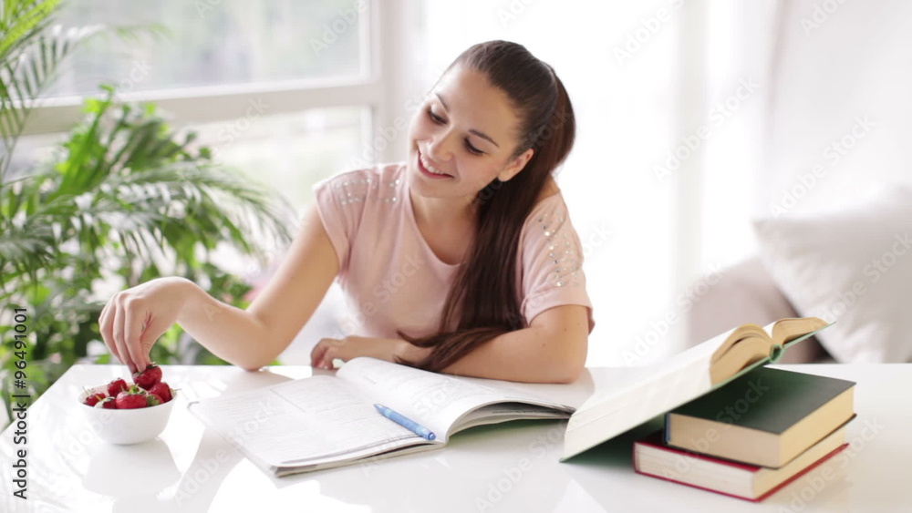 Young woman studying at table with books and eating strawberries Young woman studying at table with books and eating strawberries