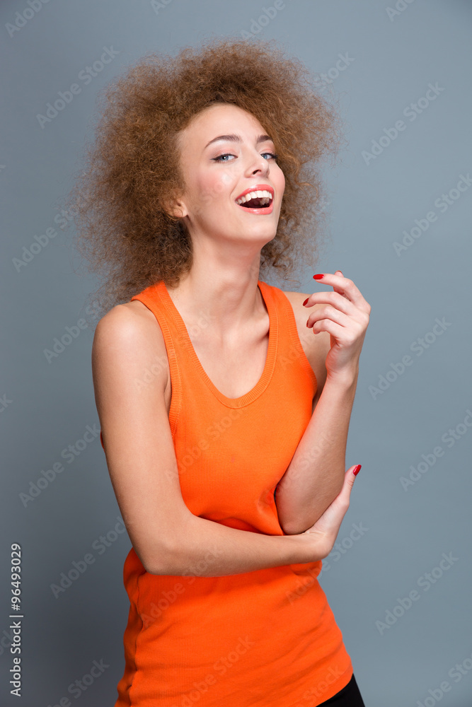 Positive laughing curly girl in orange top on gray background Positive laughing curly girl in orange top on gray background