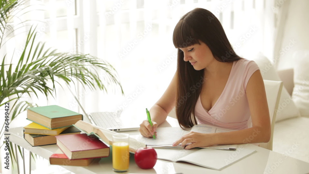 Charming girl sitting at table and studying with laptop and books Charming girl sitting at table and studying with laptop and books