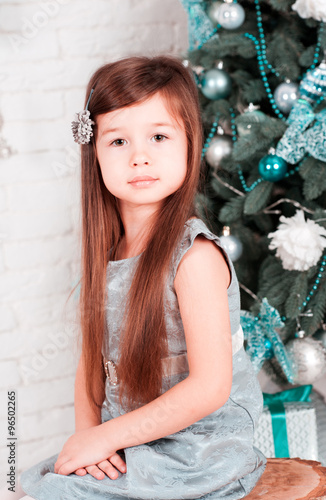 Cute baby girl 4-5 year old sitting over christmas tree in room. Looking at camera. Childhood. Christmas eve. Holiday time.  © morrowlight
