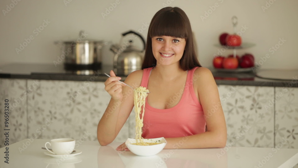 Young woman sitting at table eating noodle and smiling Young woman sitting at table eating noodle and smiling