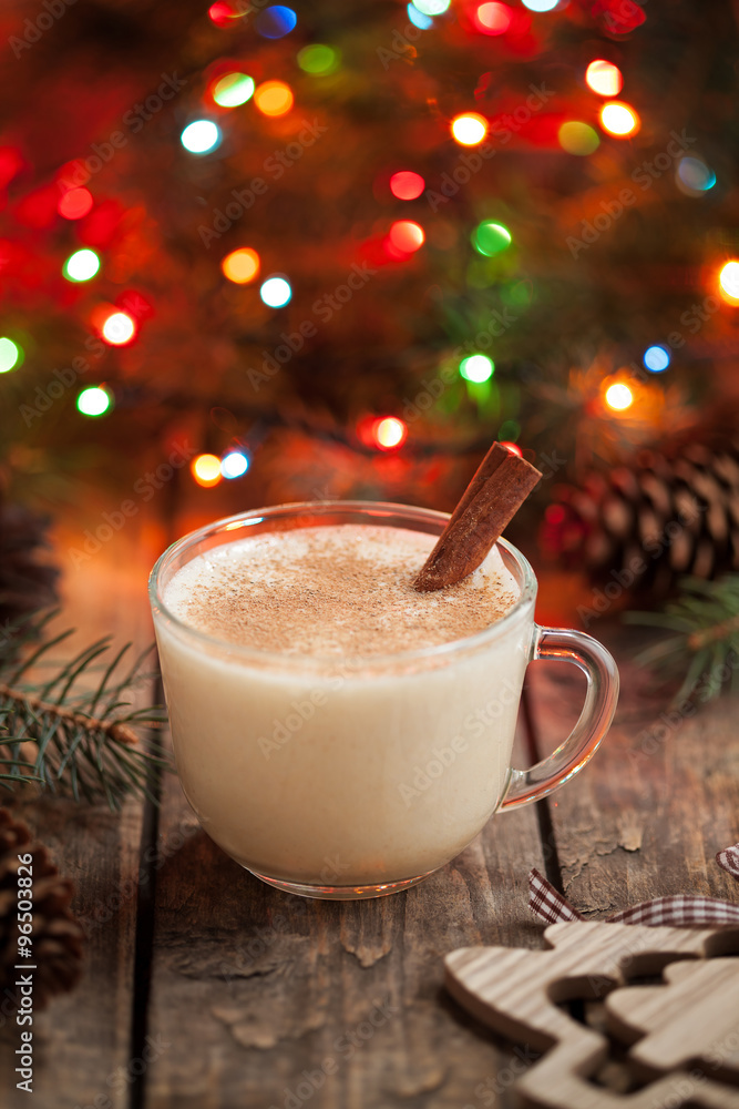 Homemade eggnog, egg milk vanilla rum, alcohol liqueur in glass with cinnamon stick on vintage wooden table. Colorful bokeh background, shallow depth of field Homemade eggnog, egg milk vanilla rum, alcohol liqueur in glass with cinnamon stick on vintage wooden table. Colorful bokeh background, shallow depth of field