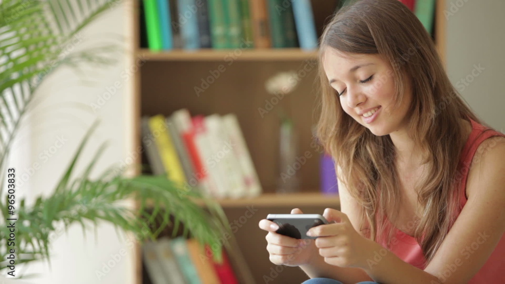 Charming girl relaxing on couch using mobile phone looking at camera and smiling Charming girl relaxing on couch using mobile phone looking at camera and smiling