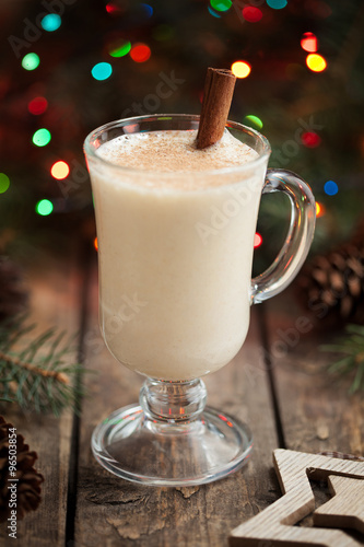 Eggnog christmass holiday traditional celebration milk cream drink in glass cup on vintage wooden table. Colorful bokeh and shallow depth of field