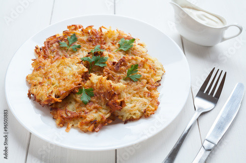 Potato pancakes or latke delicious homemade vegan food recipe with sour cream and greens on white wooden table background