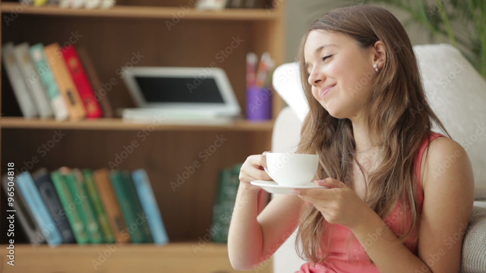 Charming girl sitting on floor drinking from cup looking at camera and smiling Charming girl sitting on floor drinking from cup looking at camera and smiling