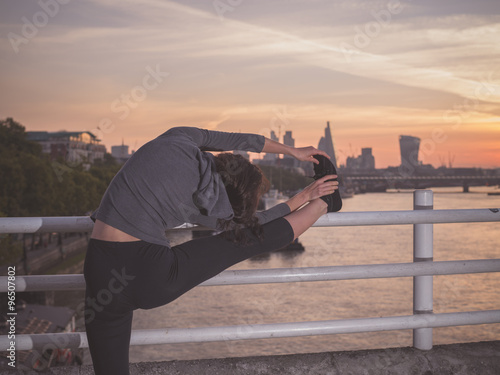 Fitness woman stretching leg on bridge at sunrise