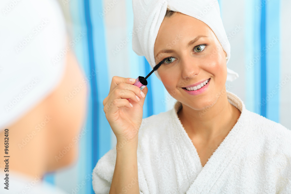 Smiling young girl in a bathrobe brushing her eyelashes in the bathroom Smiling young girl in a bathrobe brushing her eyelashes in the bathroom