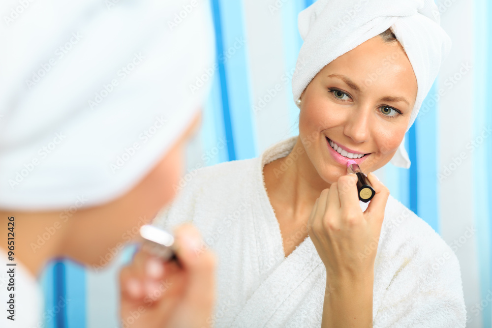 Beautiful smiling woman in a bathrobe applying lipstick in the bathroom Beautiful smiling woman in a bathrobe applying lipstick in the bathroom