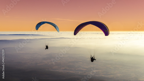 Two paragliders above a sea of clouds with a pastel sky photo
