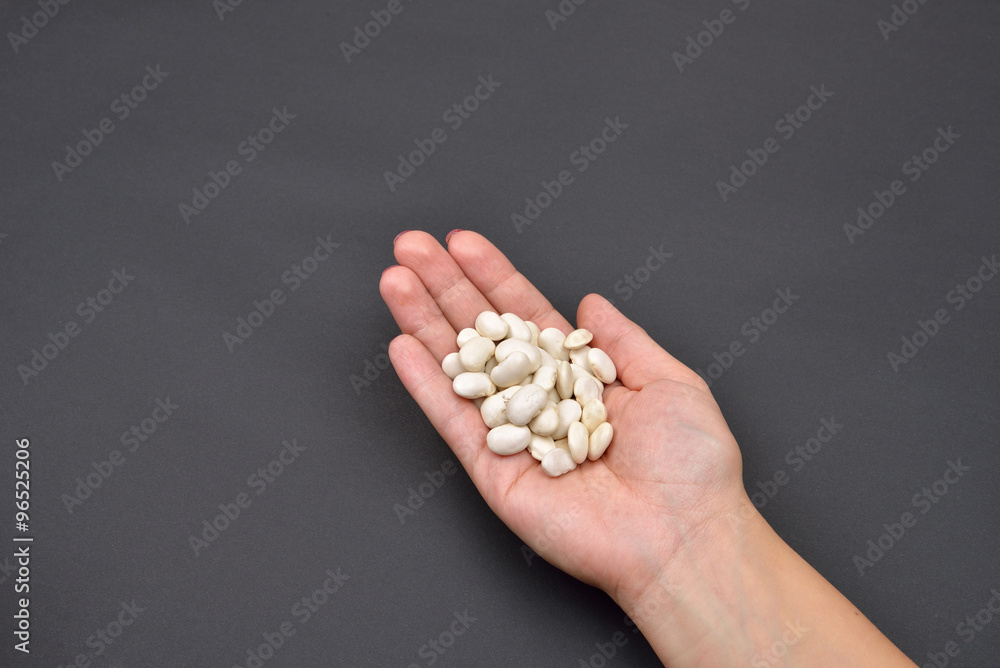 Hand of a woman holding a pile of dry white beans isolated on bl Hand of a woman holding a pile of dry white beans isolated on bl