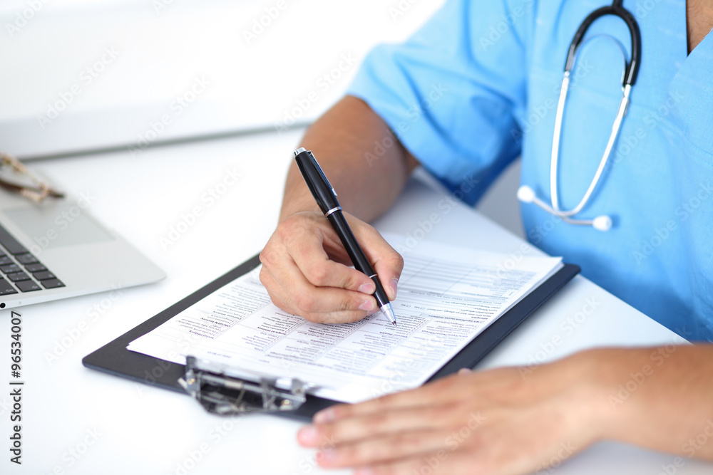 © rogerphoto - Portrait of unknown male surgeon doctor holding his stethoscope and filling up medical prescription © rogerphoto - Portrait of unknown male surgeon doctor holding his stethoscope and filling up medical prescription