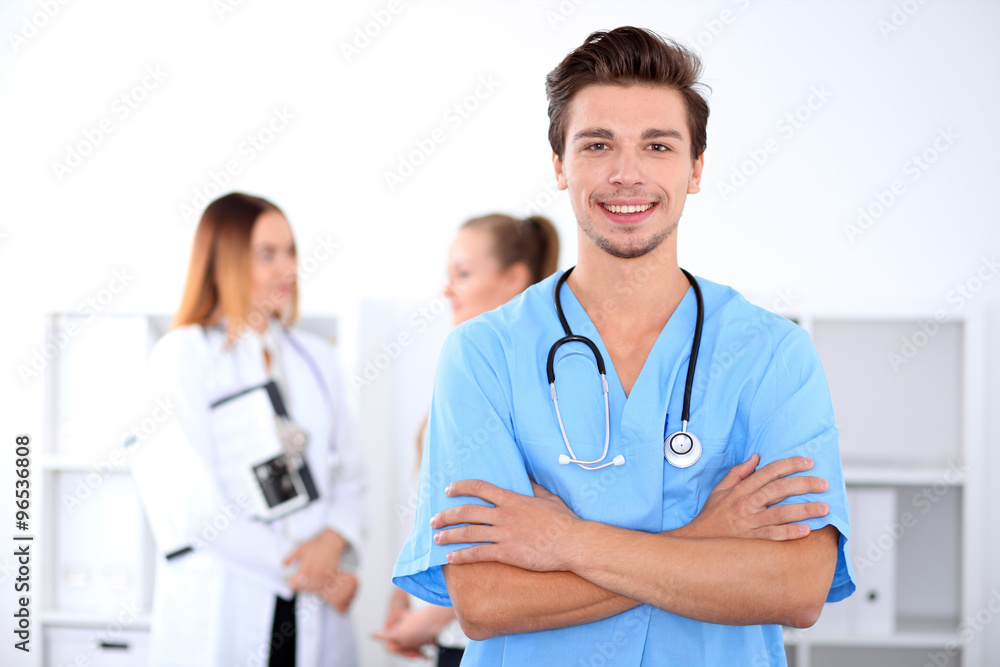 Attractive male doctor in front of medical group, crossed arms Attractive male doctor in front of medical group, crossed arms