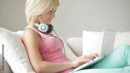 Charming young woman sitting on sifa smiling and using laptop photo