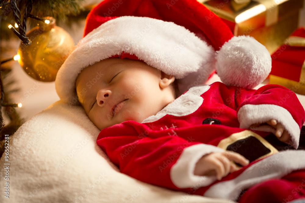 baby boy in Santa costume lying under Christmas tree. Christmas