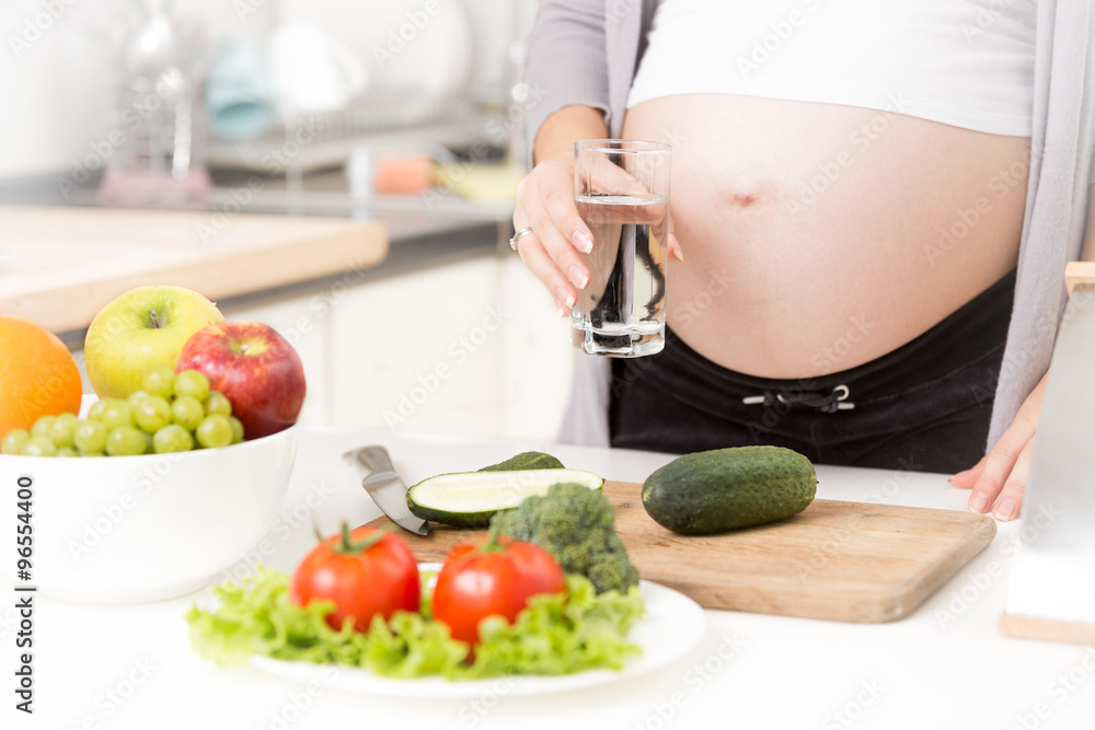 Closeup of pregnant woman holding glass of water on kitchen