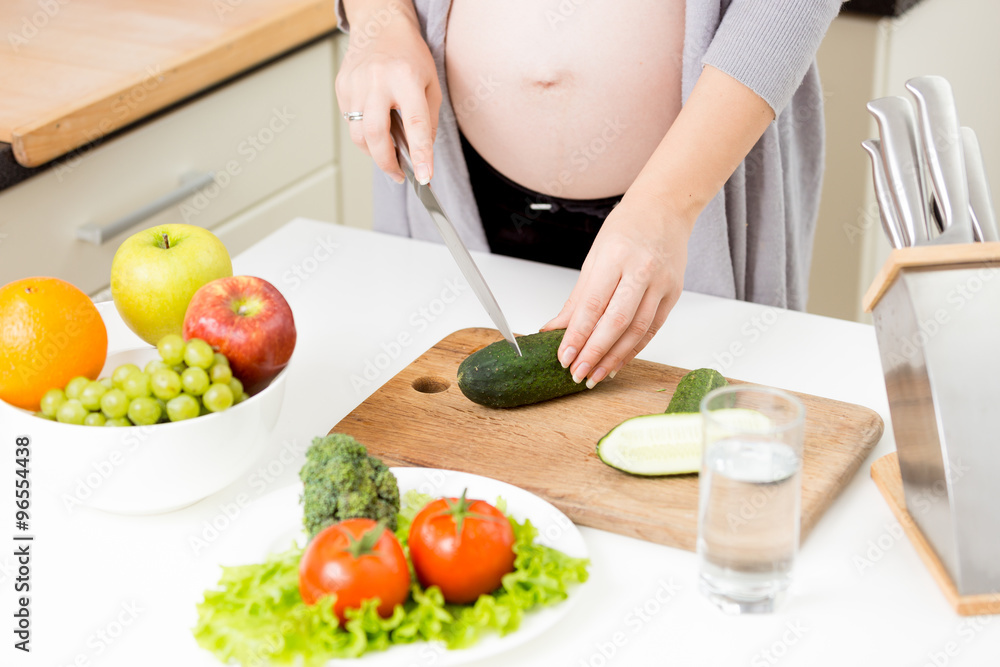 Closeup of pregnant woman making salad from vegetables Closeup of pregnant woman making salad from vegetables