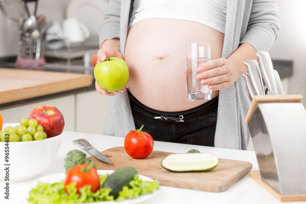 Closeup of pregnant woman having apple and water for breakfast Closeup of pregnant woman having apple and water for breakfast