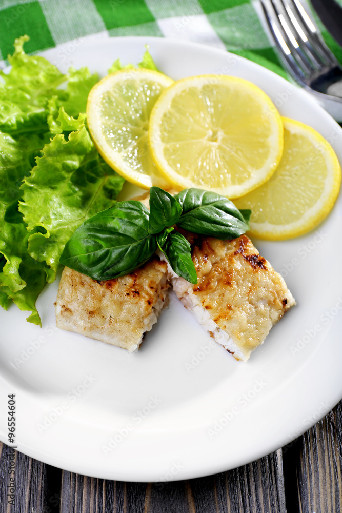 Dish of fish fillet with greens and lemon on plate close up Dish of fish fillet with greens and lemon on plate close up