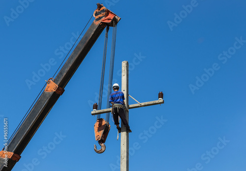 Electrician working on electric power pole with crane.