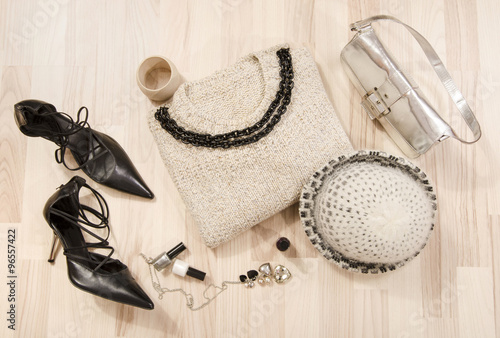 Winter sweater and accessories arranged on the floor. Woman black with silver accessories, high heels, wool hat, necklace and purse.