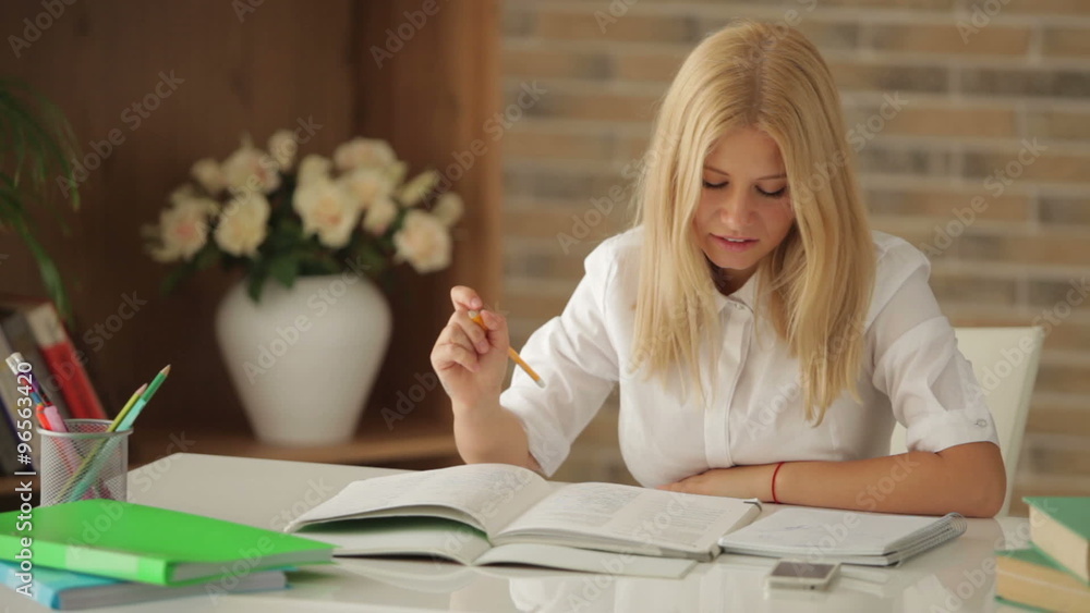 Charming girl sitting at desk studying writing in notebook looking at camera and smiling Charming girl sitting at desk studying writing in notebook looking at camera and smiling