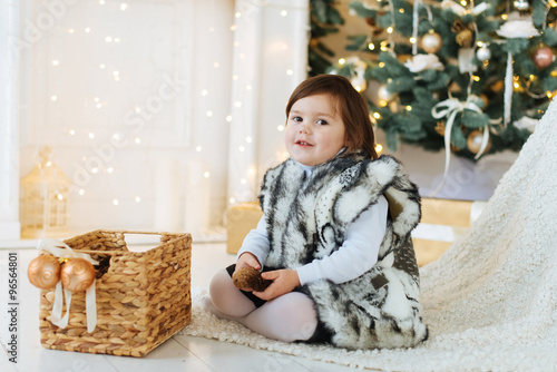 Little smiling girl  near the Christmas tree and gifts. 