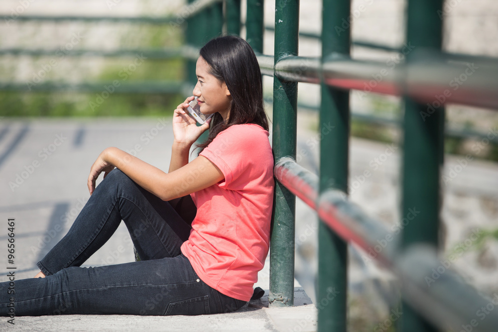 Young Asian student outdoor, talking on the phone while sitting