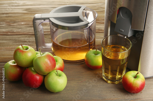Stainless juice extractor with apples on wooden background, close up
