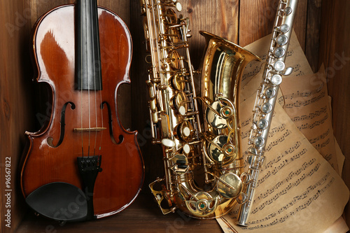 Canvas Print Musical instruments: saxophone, violin and flute with notes on wooden background