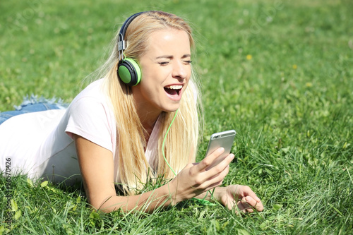 Young woman with earphones and smartphone listening to music on grass