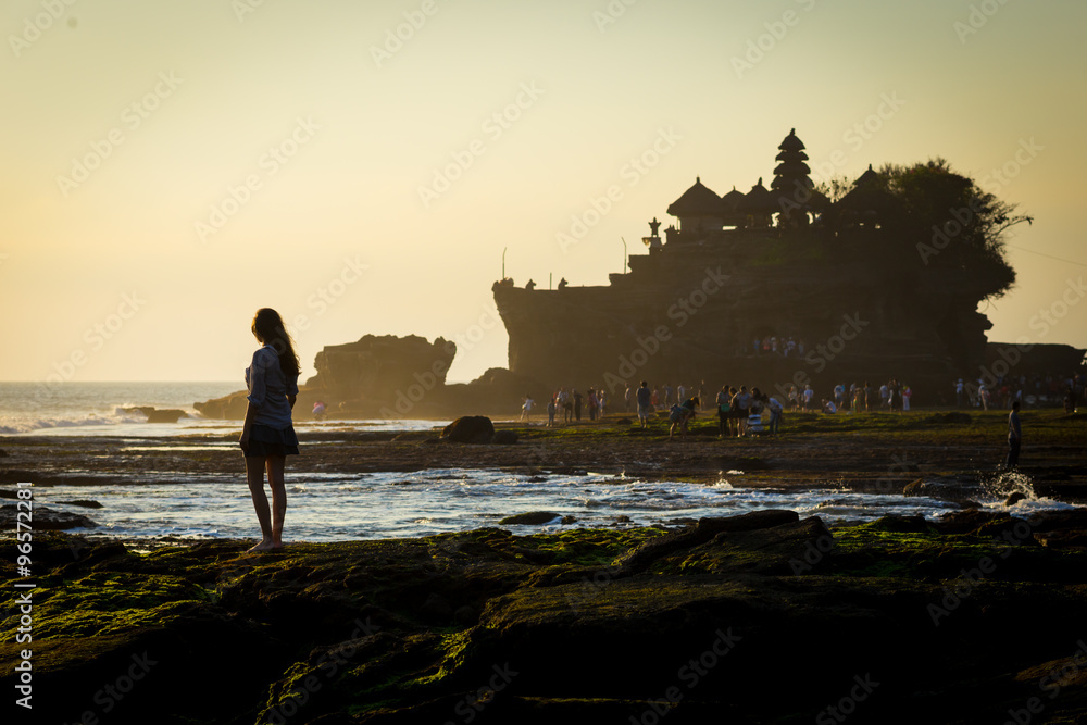 Young woman walking a ocean coastline with the hindu temple Pura Tanah Lot in background, Bali, Indonesia