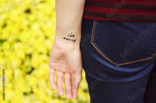Hand of young woman with tattooed phrase on it, on yellow flowers background, close-up