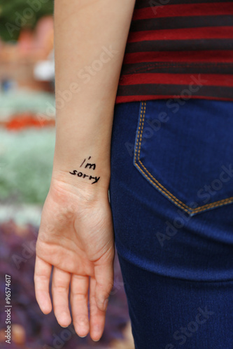 Hand of young woman with tattooed phrase on it, on flowers background, close-up © Africa Studio