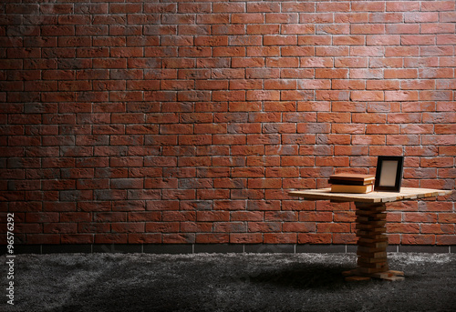 Small wooden table, books and a photo frame on red brick wall background