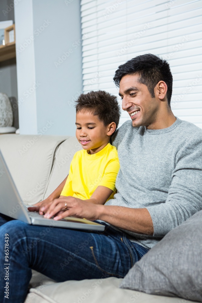 Smiling father and son using laptop on the sofa Smiling father and son using laptop on the sofa