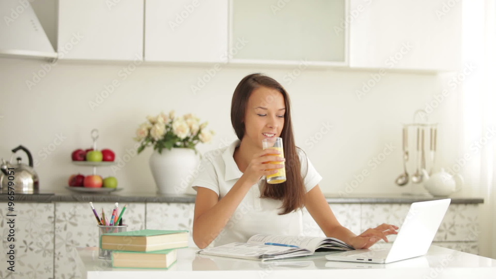 Cheerful student girl sitting at table using laptop drinking juice and smiling Cheerful student girl sitting at table using laptop drinking juice and smiling